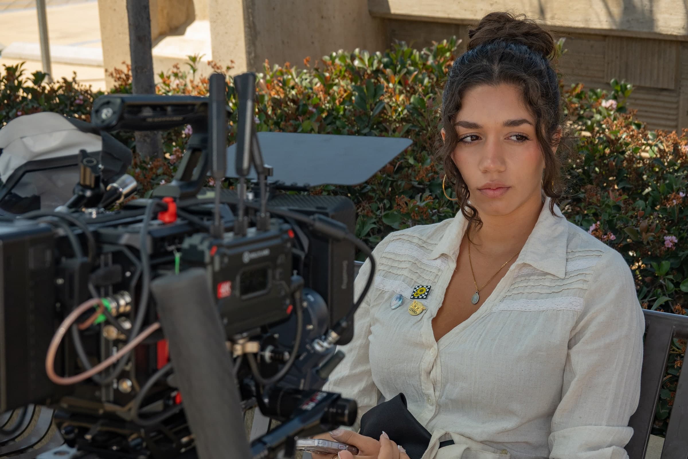 Emily Loaiza seated on a bench beside a cinema camera rig, outdoors