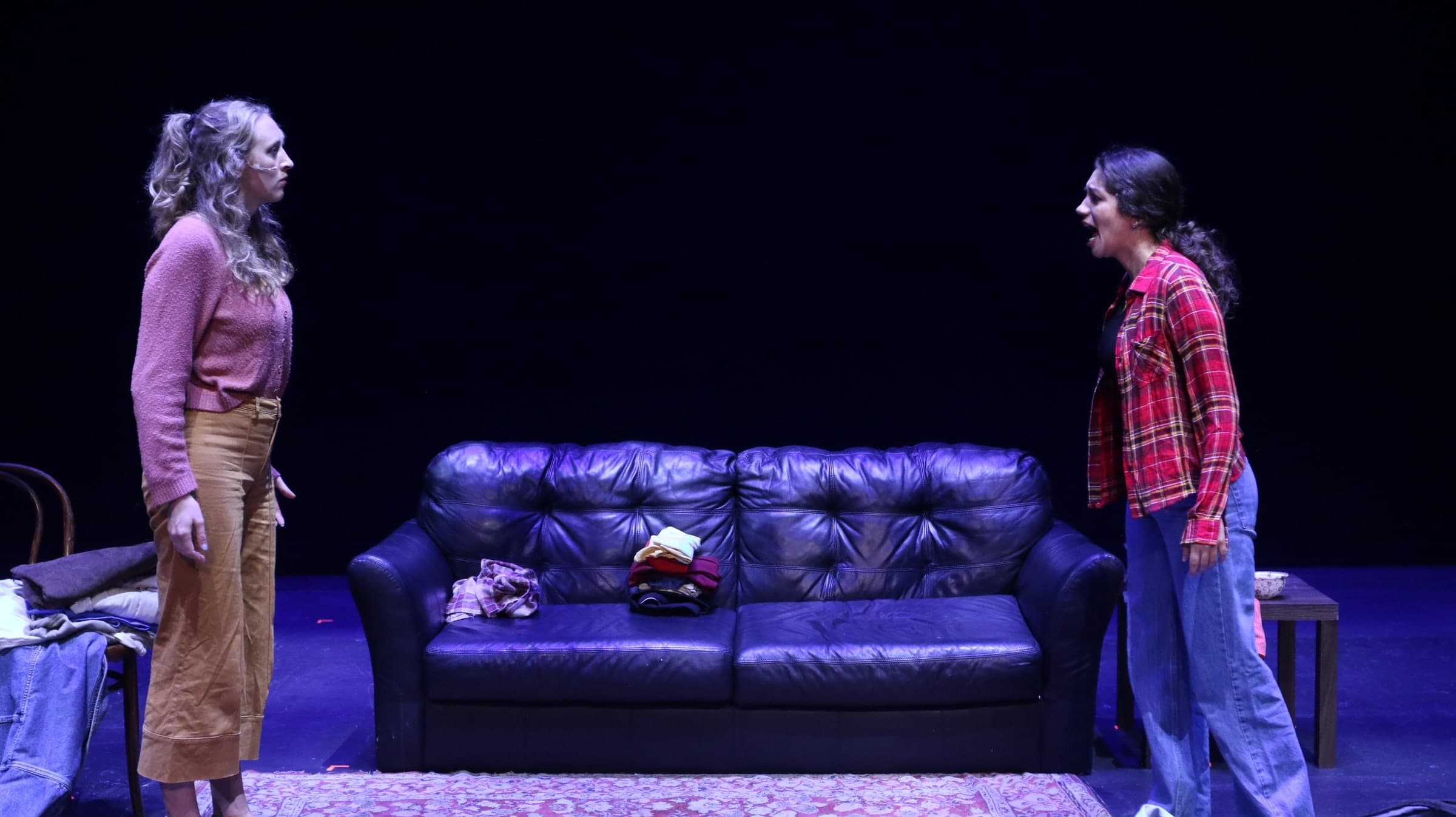 Emily Loaiza confronting a scene partner across a sofa on stage