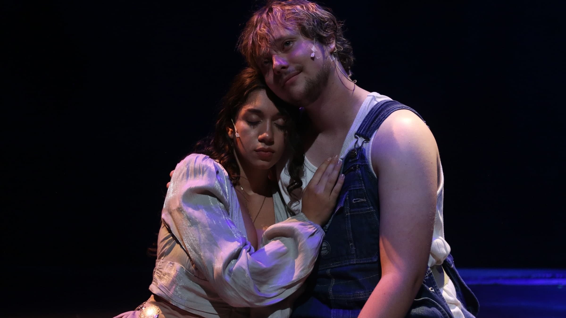 Emily Loaiza resting her head on a scene partner’s shoulder on stage