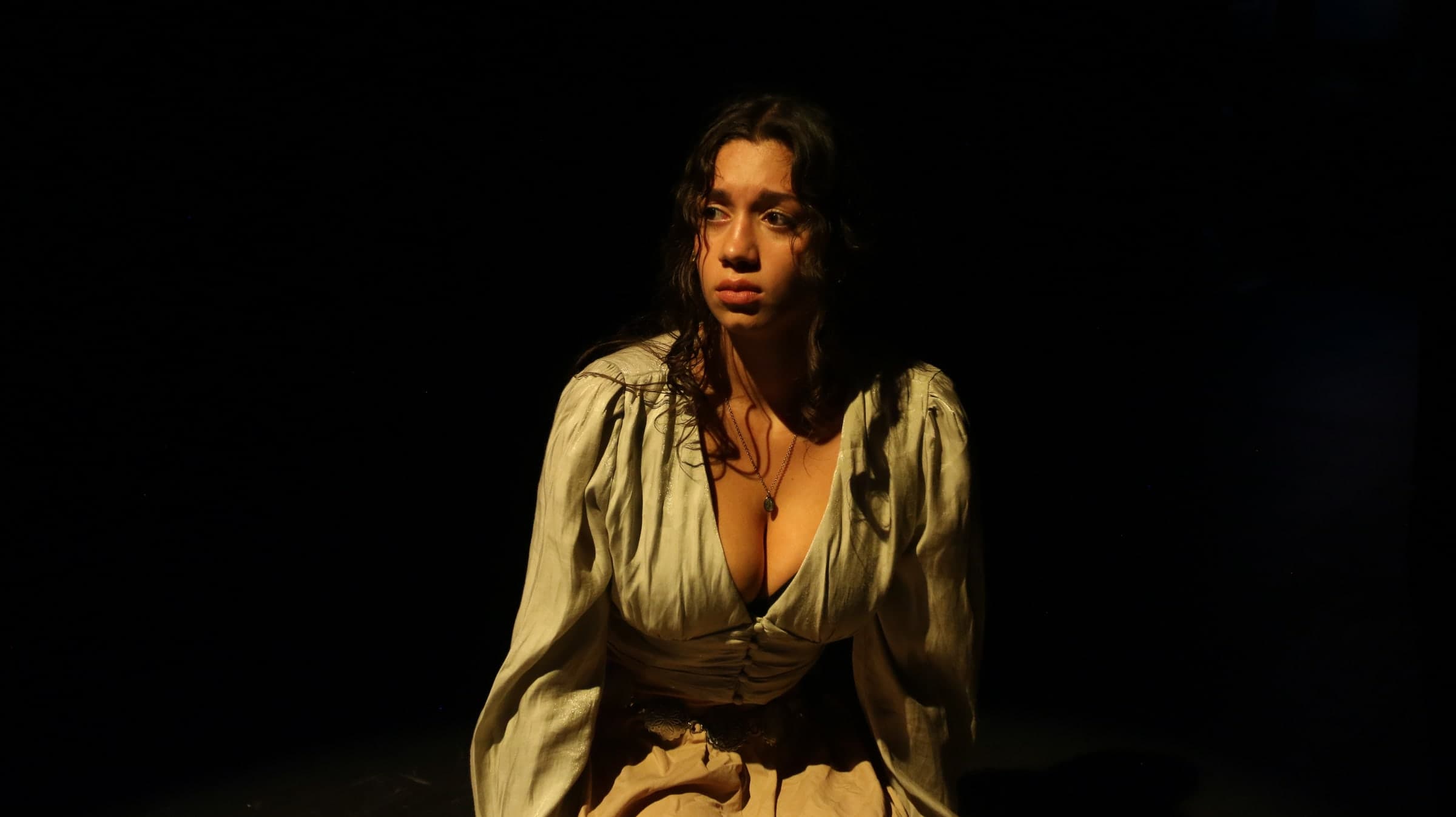 Emily Loaiza kneeling in an amber spotlight on stage