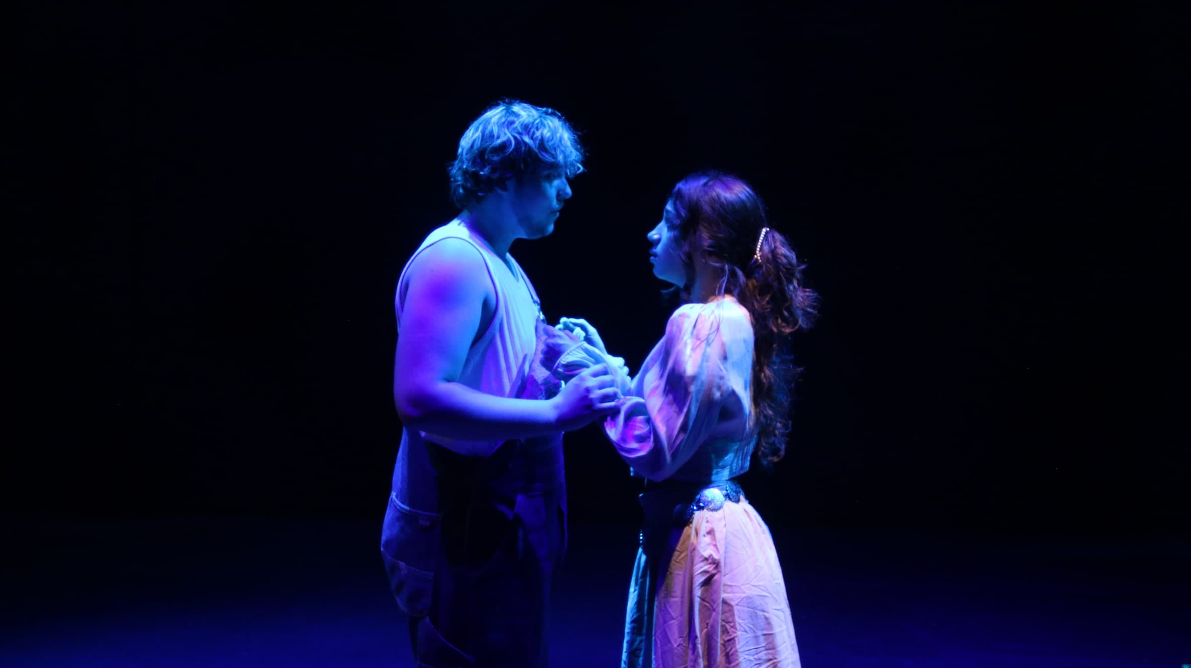 Two actors holding hands under violet stage light